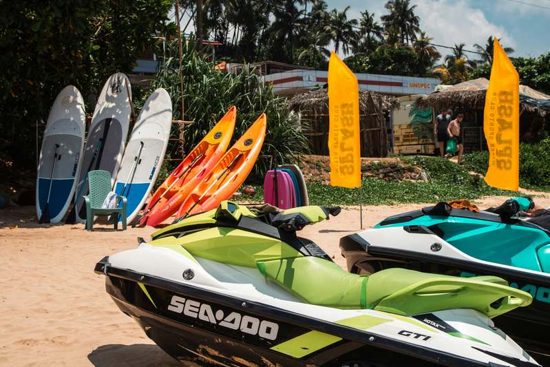 Diverse group of kayak rental operators reviewing documents and checking gear near a sunlit marina dock